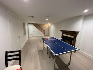 Une pièce avec une table de ping-pong, une cheminée et un escalier.