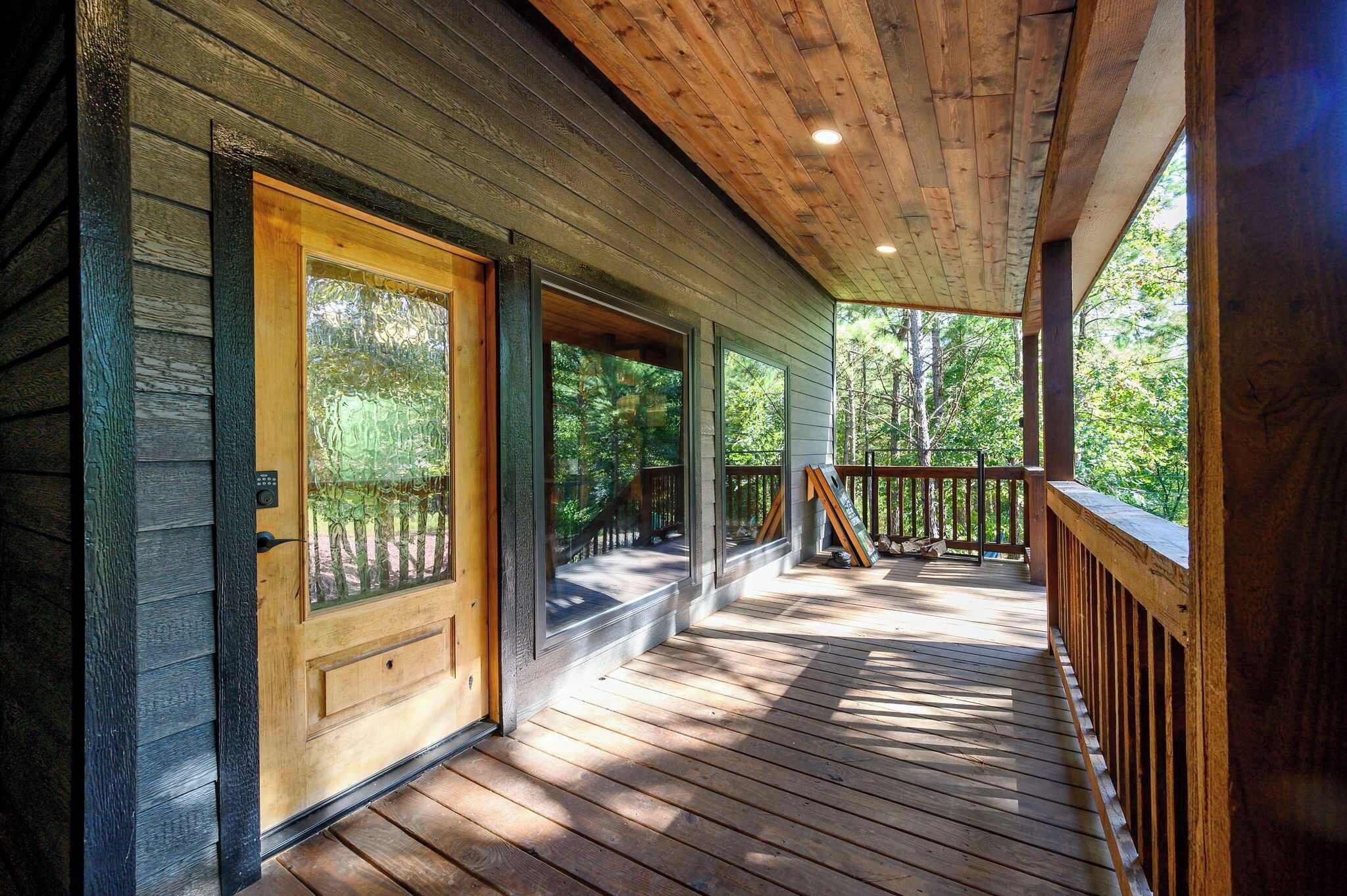 A wooden porch with a glass door and windows, leading to a deck with a railing.