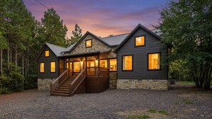 A two-story log cabin with a stone foundation, a wooden staircase, and a gravel driveway. - Sweet Magnolia - 3BR Cozy Cabin (Broken Bow)