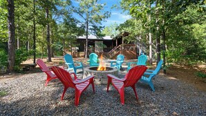 A fire pit surrounded by Adirondack chairs in a forest setting. - Sweet Magnolia - 3BR Cozy Cabin (Broken Bow)