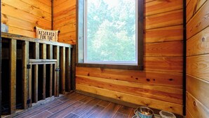 A wooden cabin interior with a window, a metal gate, and a pet feeding station. - Sweet Magnolia - 3BR Cozy Cabin (Broken Bow)