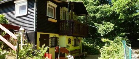 A two-story house with a balcony, surrounded by greenery.