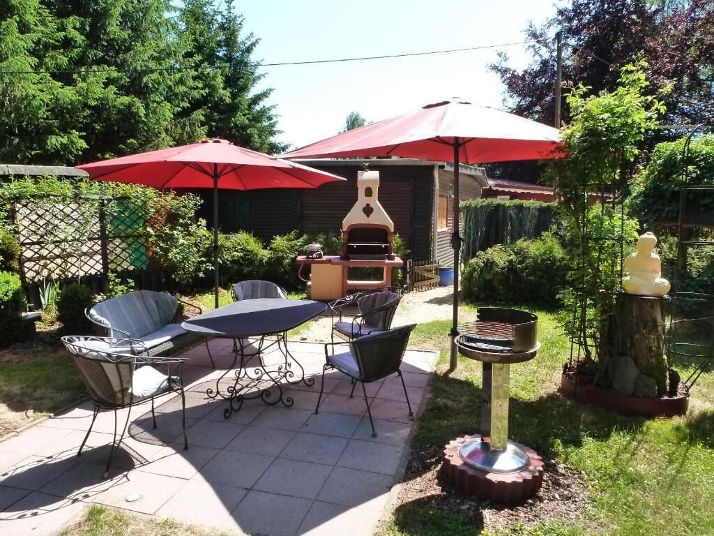 An outdoor patio with a grill, dining table, and chairs, surrounded by greenery and umbrellas.