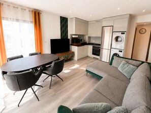 A modern living space with a dining area, a sofa, a TV, a kitchen, and a washing machine. - Spacious, modern apartment—near Metro Line 7 (Aubervilliers)