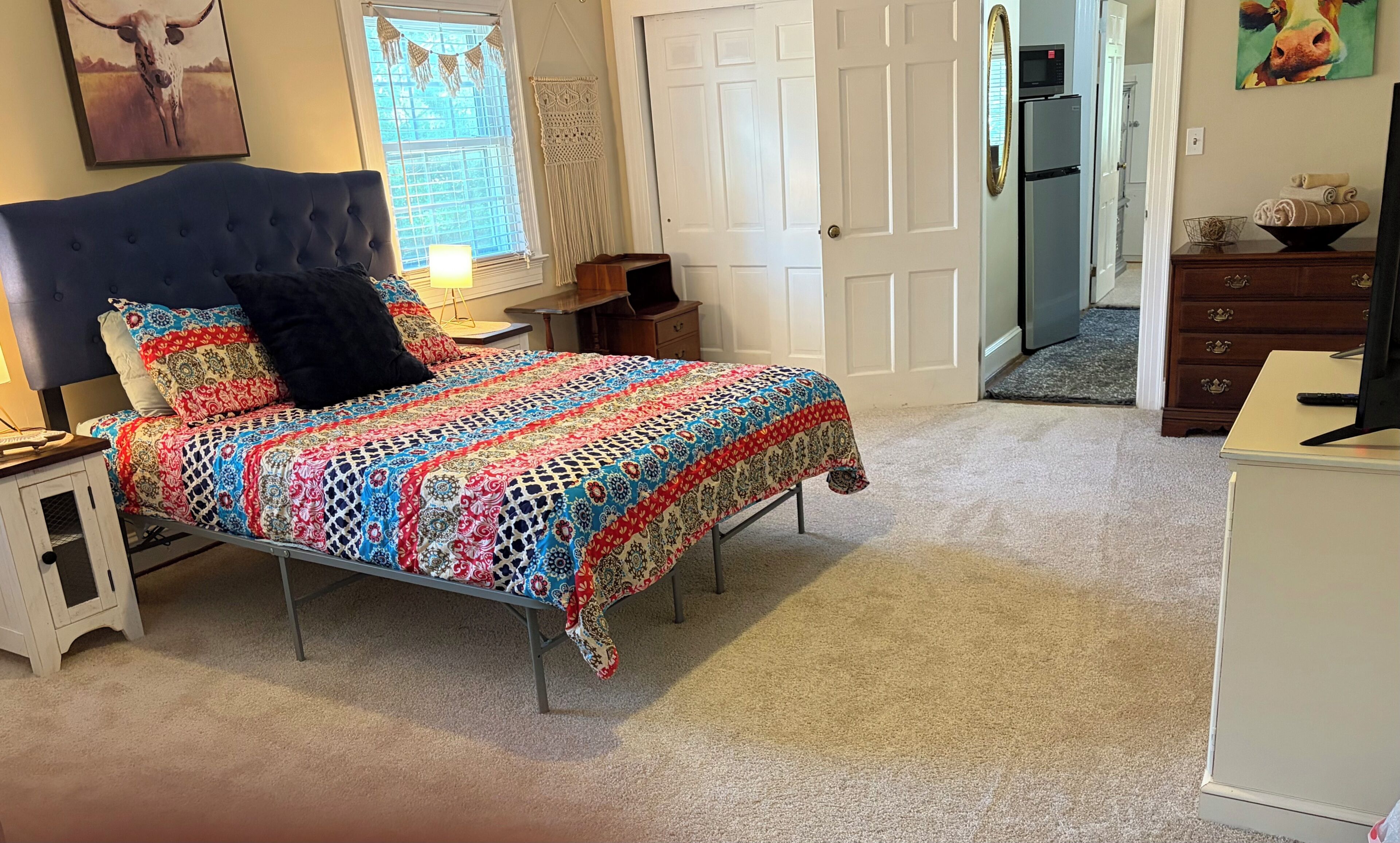 A bedroom with a bed, bedside tables, a dresser, a door, and a window.