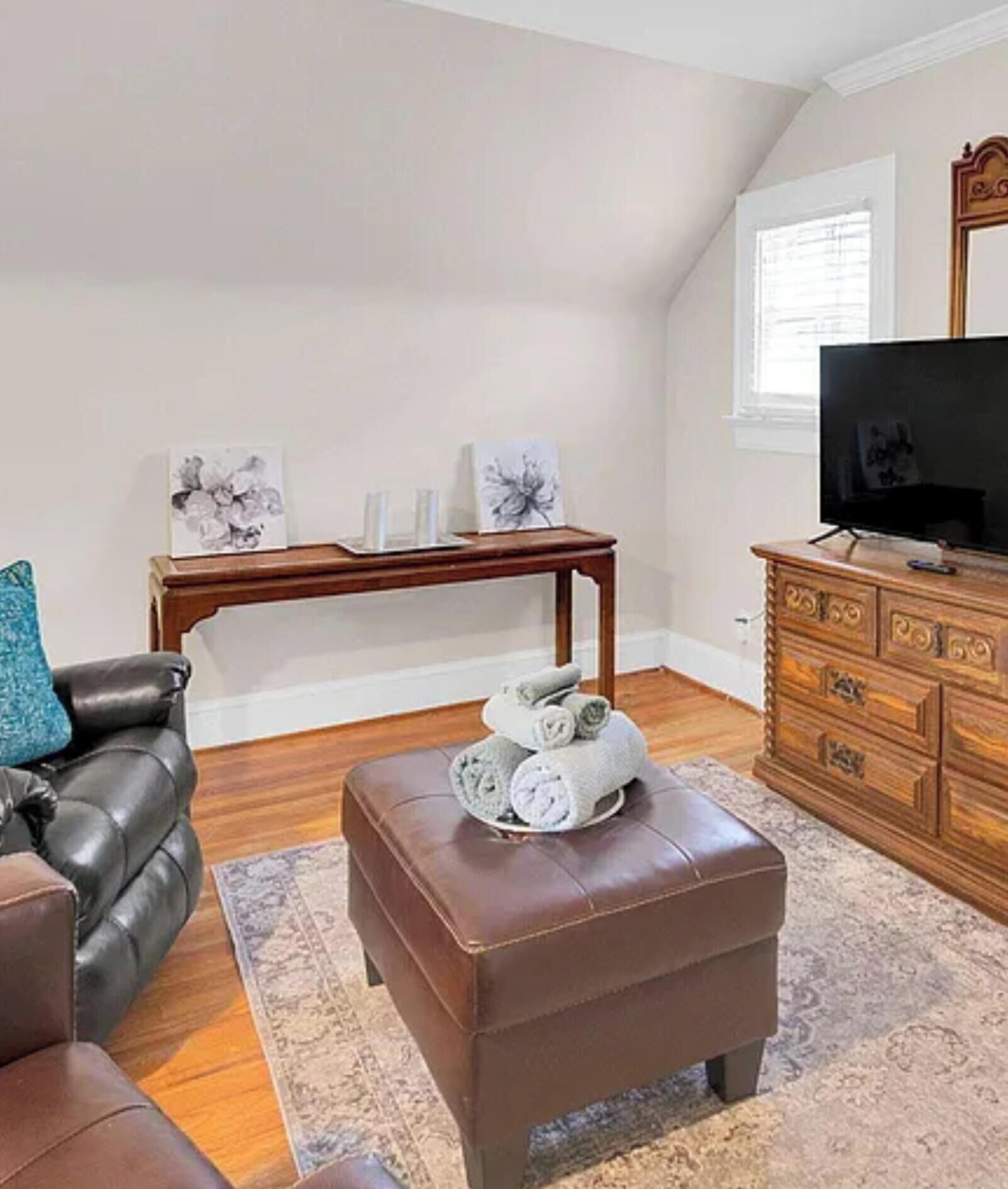 Een woonkamer met een bruine leren bank, een houten salontafel, een bruin voetenbankje, een houten dressoir en een televisie.