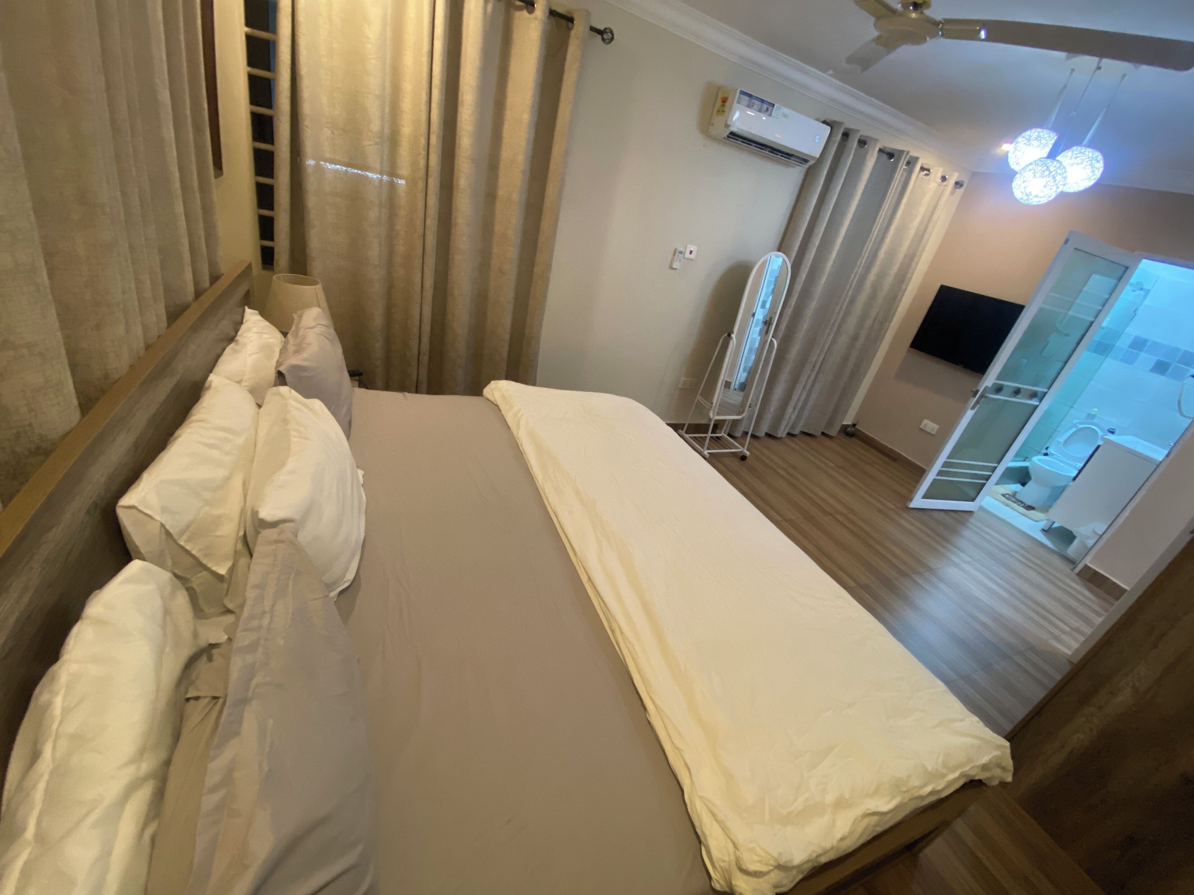 Ein Hotelzimmer mit Bett, Vorhängen, einer Klimaanlage, einem Deckenventilator und Blick ins Badezimmer.