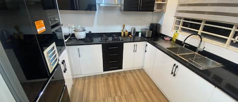 Cozinha moderna com armários preto e branco, pia de aço inoxidável e piso de madeira.