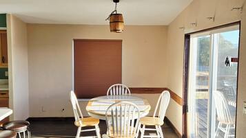 A dining area with a round table, white chairs, and a wooden ceiling light fixture.