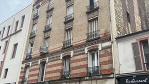 A multi-story building with a ground-floor entrance, a sign indicating a restaurant, and a row of parked scooters. - Simple, affordable studio apartment near Paris (Clichy)
