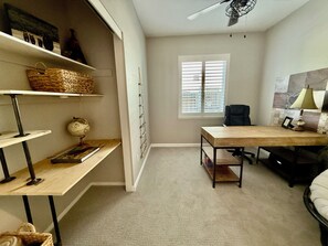 A room with a desk, chair, shelves, a window, and a ceiling fan.