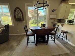 A dining area with a round table, chairs, a chandelier, and a view of the outdoors.