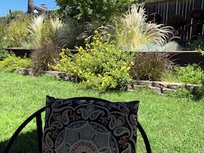 A garden with a patterned cushion on a chair, surrounded by various plants and a wooden fence.