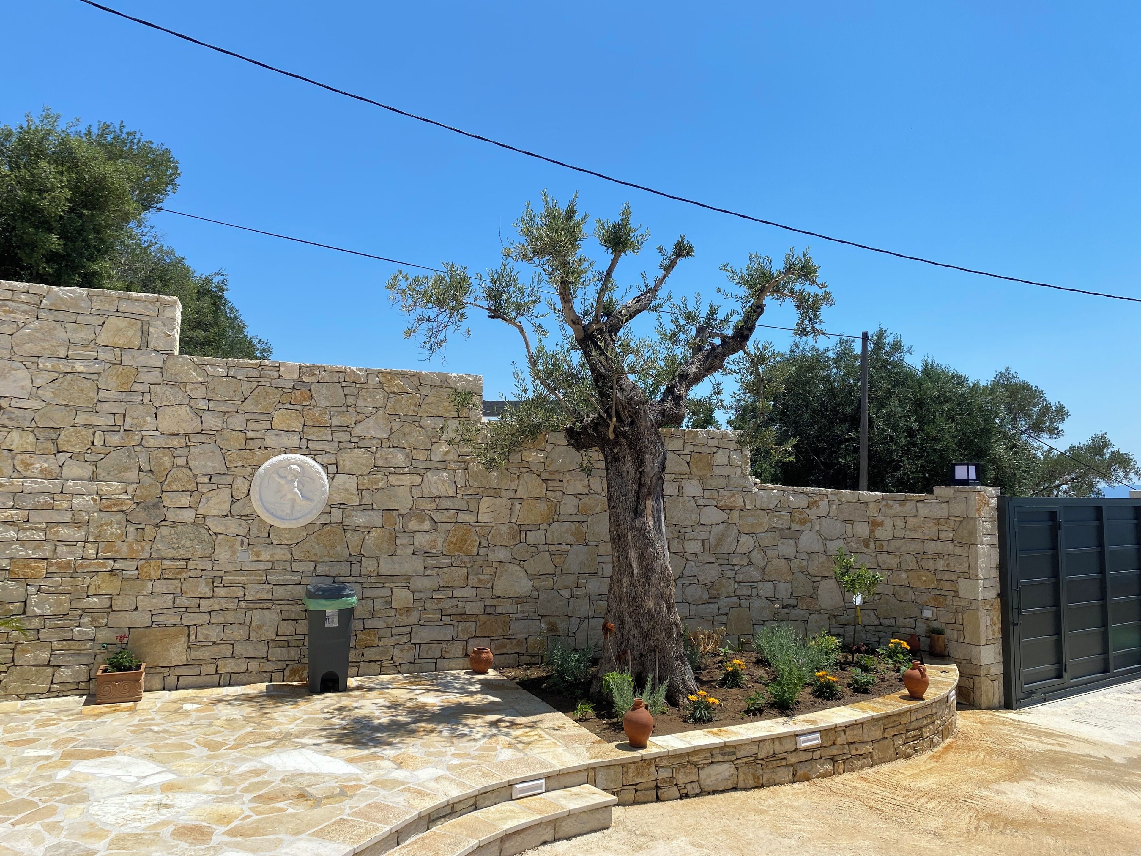 Un mur de pierre orné d’une plaque circulaire, un arbre et un jardin avec des fleurs et un vase.