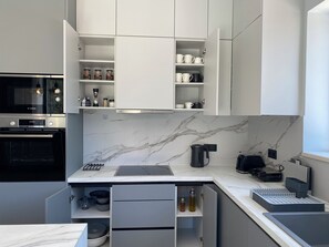 Eine moderne Küche mit weißen Schränken, einem Bosch-Ofen, einer Marmor-Spritzschutzleiste und einer Kaffeemaschine.