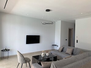 Ein modernes Wohnzimmer mit Fernseher, einer Couch, einem Couchtisch und einem Sessel.