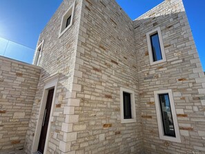 Eine Gebäudeecke mit steinverkleideter Fassade, zwei Fenstern und einer Tür.