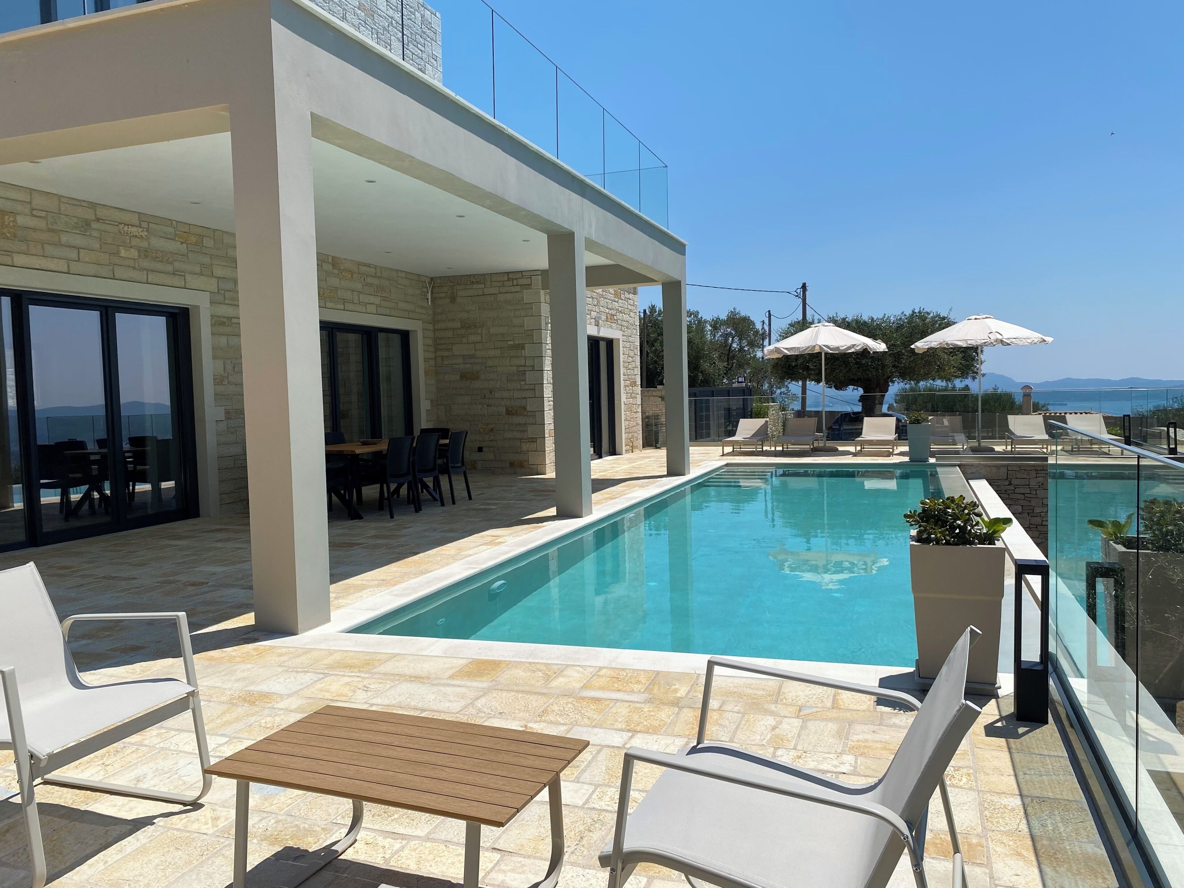 A modern outdoor pool area with a clear view of the sea, a covered seating area, and a table.