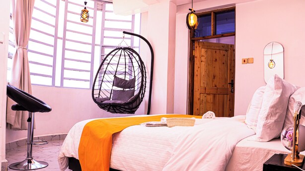 A bedroom with a bed, a hanging chair, a wooden door, and a window with curtains. - Luxury Kimana Stay Near Amboseli (Kimana)