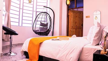 Un dormitorio con cama, una silla colgante, una puerta de madera y una ventana con cortinas.