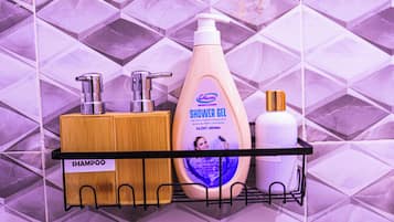Un estante de baño con un jabonera de madera, una botella dosificadora de gel de ducha y una botella blanca.