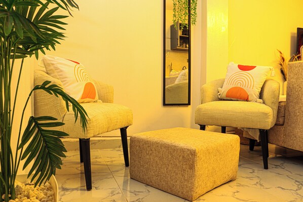 A room with two armchairs, a small ottoman, a potted plant, and a mirror on the wall.