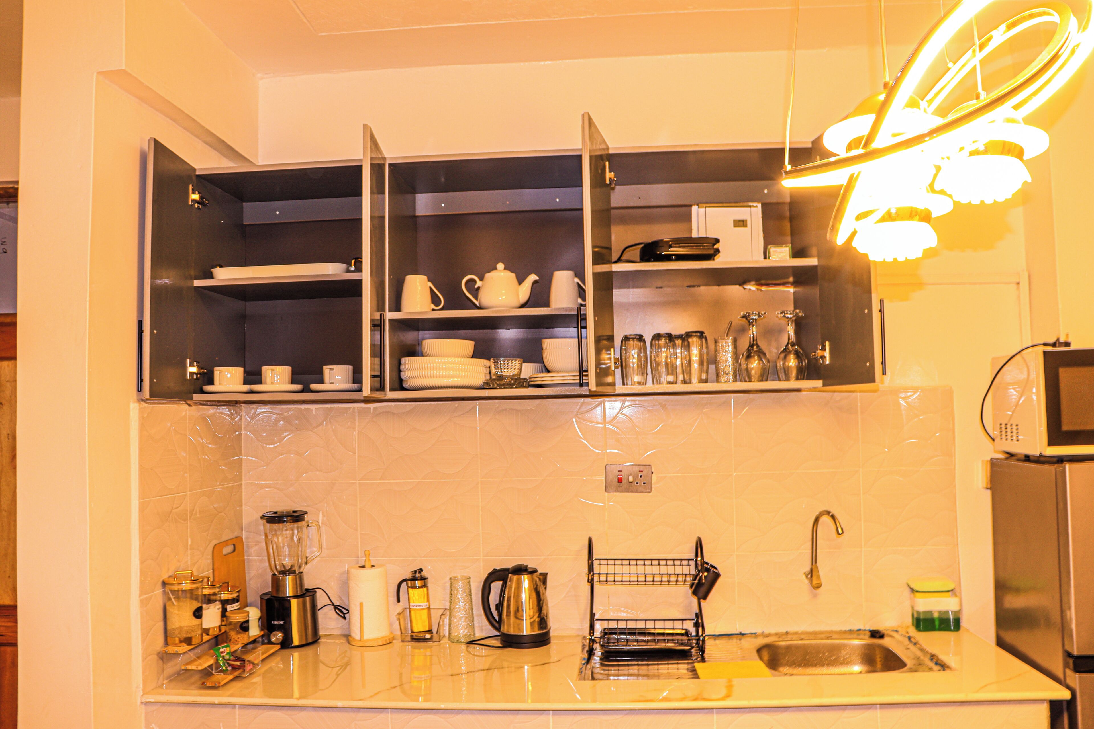 Una cocina con armarios abiertos, un lavamanos y diversos electrodomésticos.