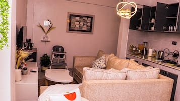 Un espacio habitable compacto con kitchenette, un conjunto de sofás, una mesa de comedor y una televisión.