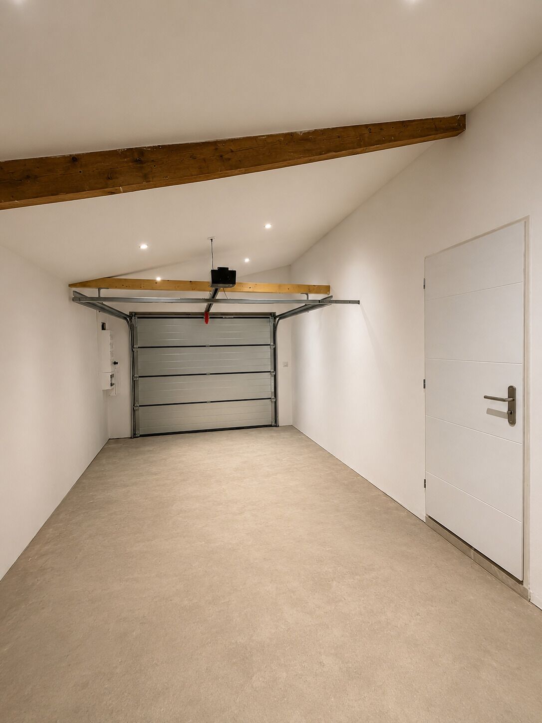 A garage with a closed metal door, a ceiling-mounted projector, and a white door on the right.