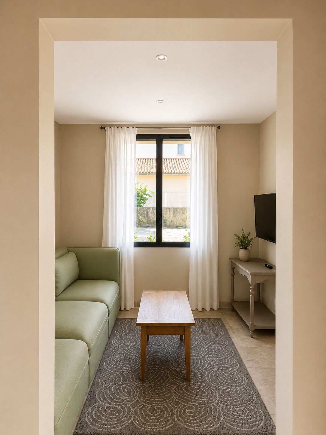 A room with a green sofa, a small wooden table, a TV on a stand, and a window with curtains.
