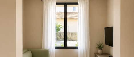 A room with a green sofa, a small wooden table, a TV on a stand, and a window with curtains.
