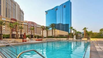 A hotel with a swimming pool, palm trees, and modern buildings in the background.