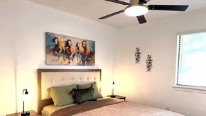 Un dormitorio con cama, ventilador de techo, un cuadro y dos mesitas de noche.