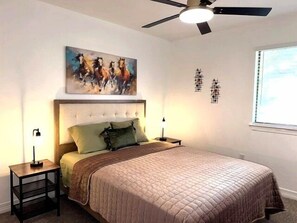 Una camera da letto con un letto, una ventola a soffitto, un quadro e due comodini.