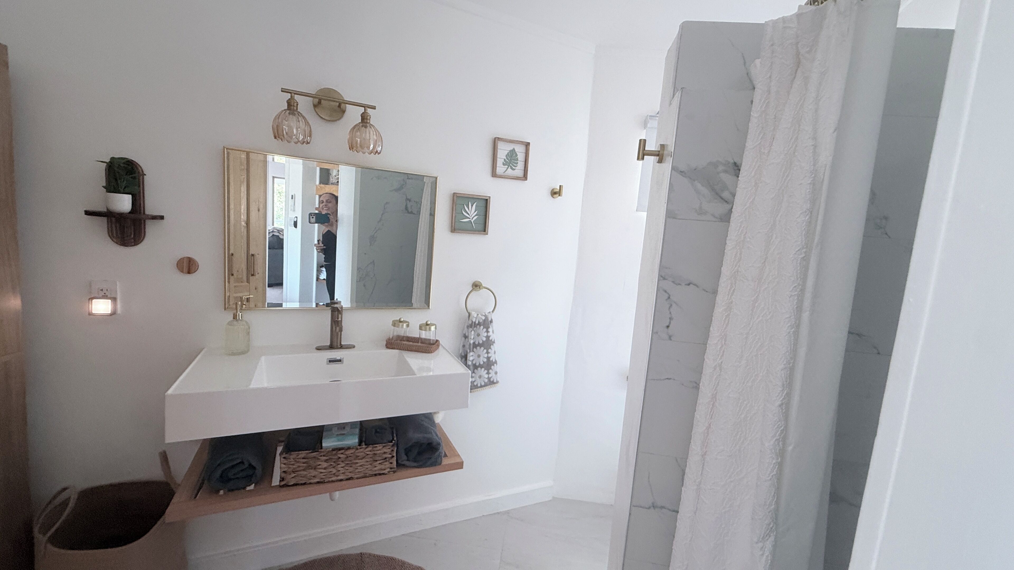Un baño con tocador blanco, un espejo grande, toallero y cortina de ducha.