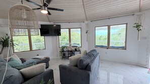 Amplia sala de estar con ventilador de techo, ventanas grandes y televisor de pantalla plana montado en la pared.