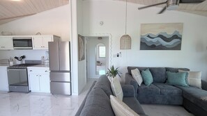 A modern kitchen with a refrigerator, stove, and cabinets. There is a gray sofa with cushions and a plant in the living area.