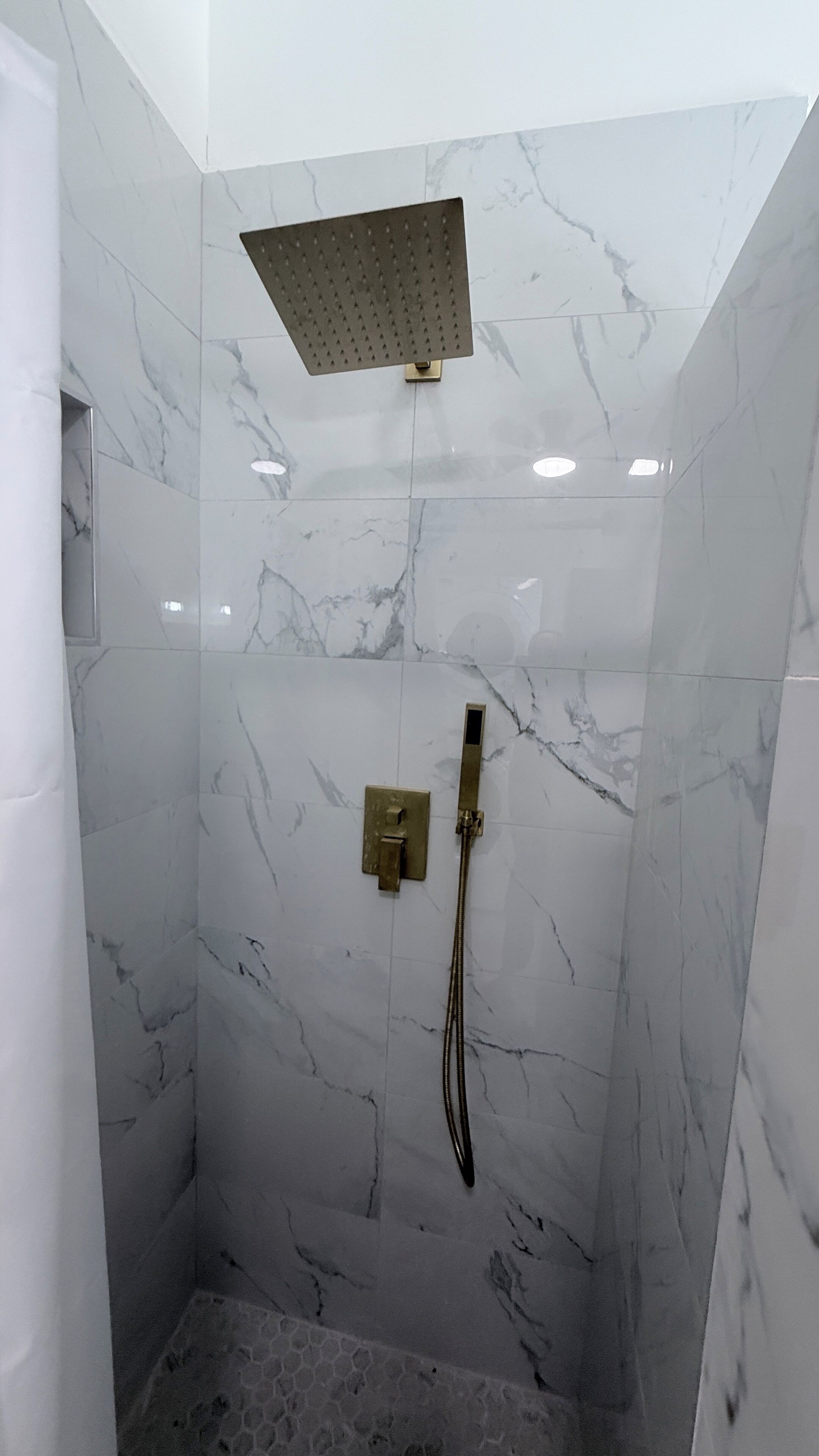 A shower area with a square showerhead, a handheld showerhead, and a control panel.