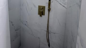 A shower area with a square showerhead, a handheld showerhead, and a control panel.