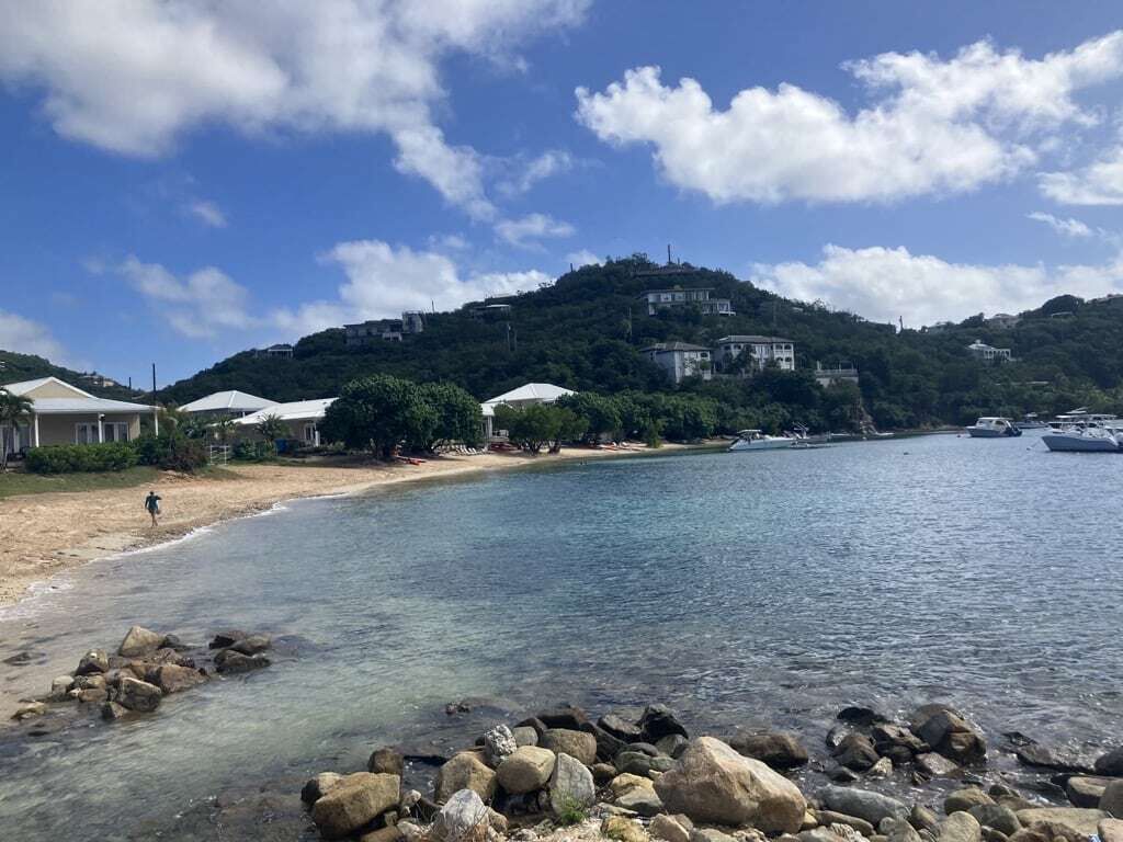 Une zone côtière avec une plage de sable fin, une côte rocheuse et des bâtiments situés sur une colline en arrière-plan.