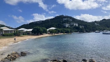 Une zone côtière avec une plage de sable fin, une côte rocheuse et des bâtiments situés sur une colline en arrière-plan.