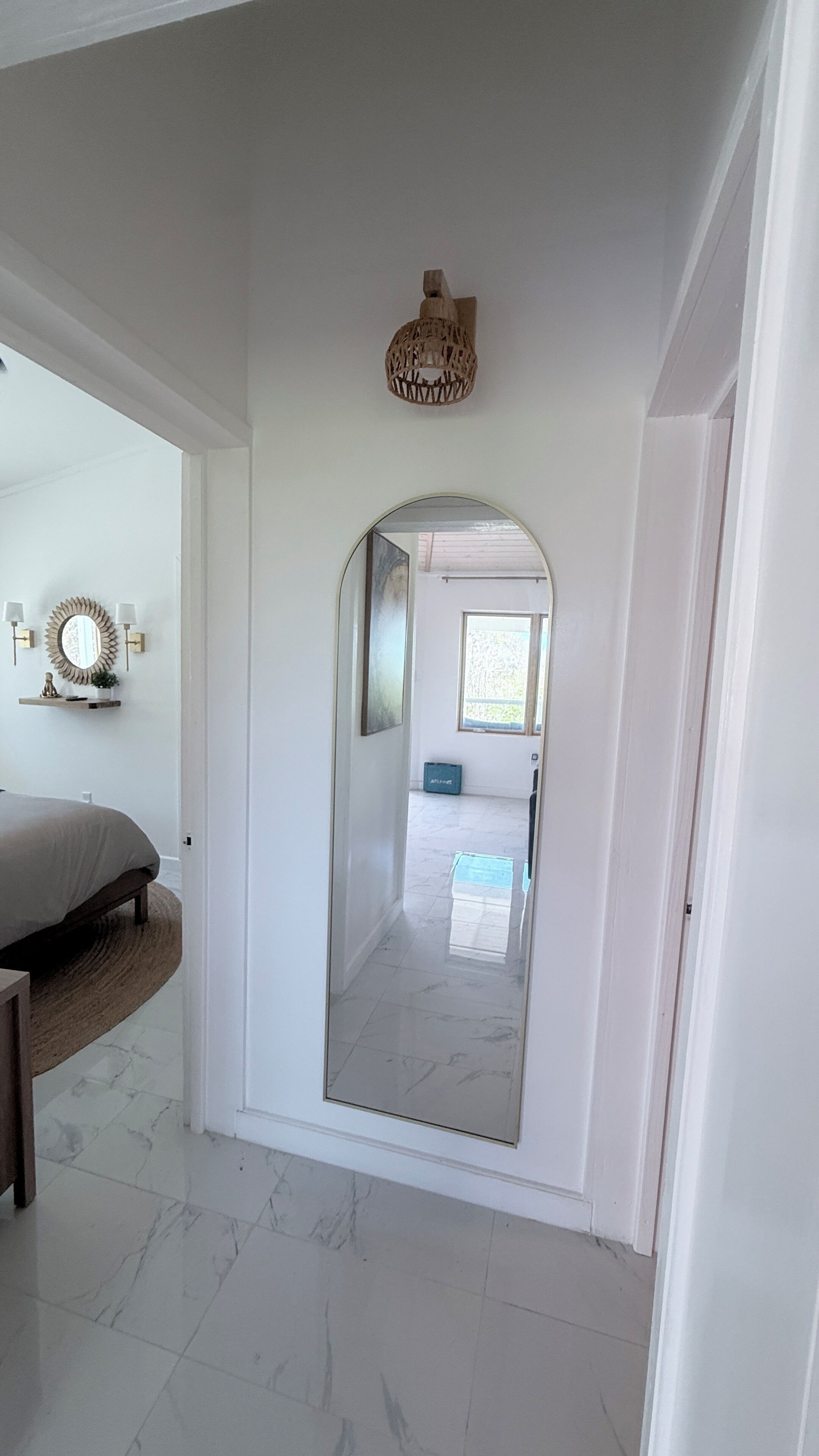 Un couloir avec un grand miroir, un lit et un luminaire fixé au plafond.