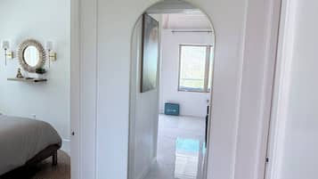 Un couloir avec un grand miroir, un lit et un luminaire fixé au plafond.