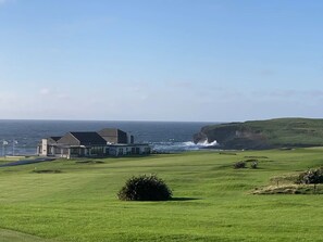 A coastal property with a grassy lawn, a building with a sloped roof, and a view of the sea.