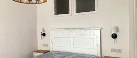 A bedroom with a bed, two windows, a headboard, bedside tables, and a lamp.