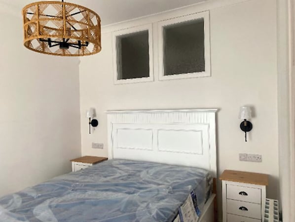 A bedroom with a bed, two windows, a headboard, bedside tables, and a lamp.