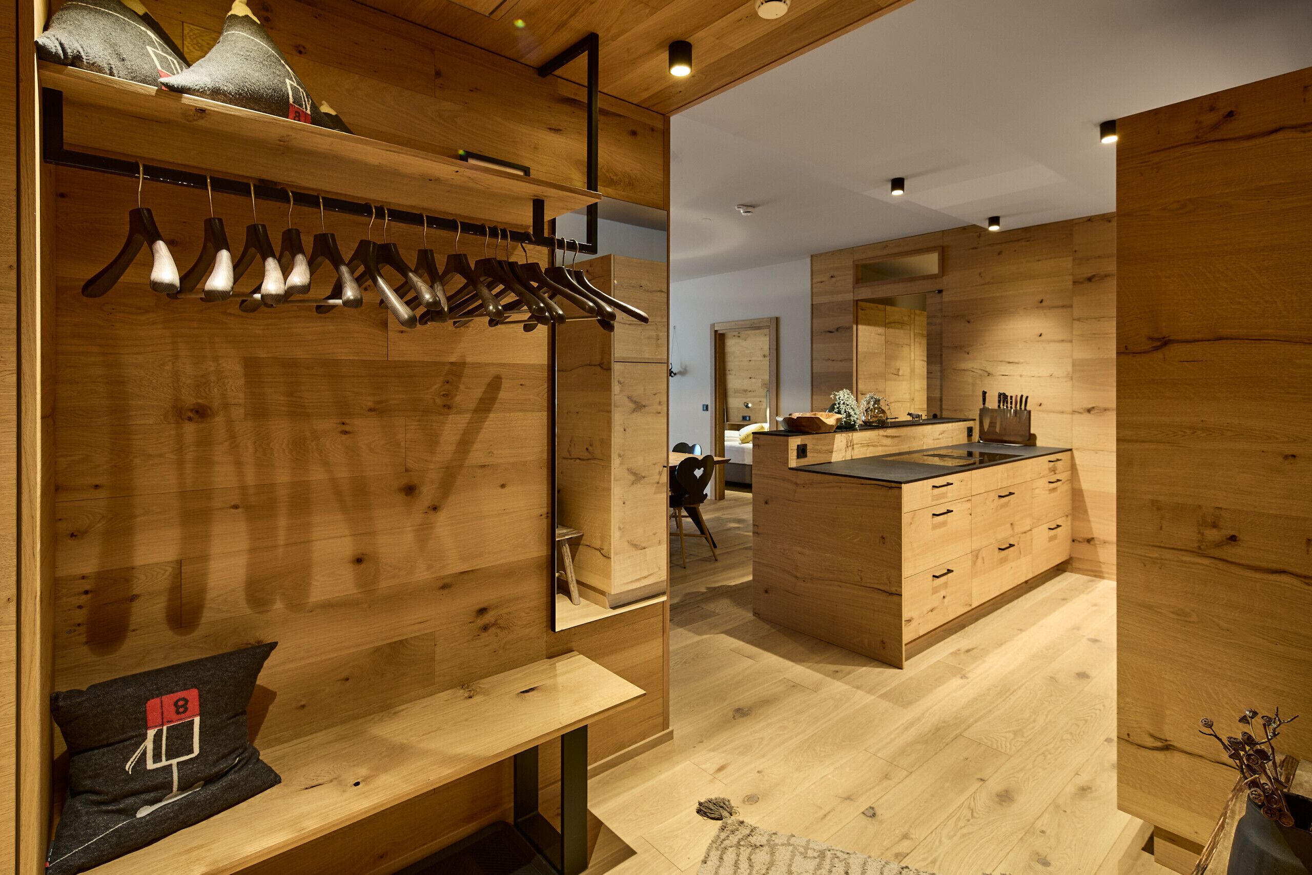 Een houten interieur met een kledingrek, een bankje, een spiegel en een keukenhoek.