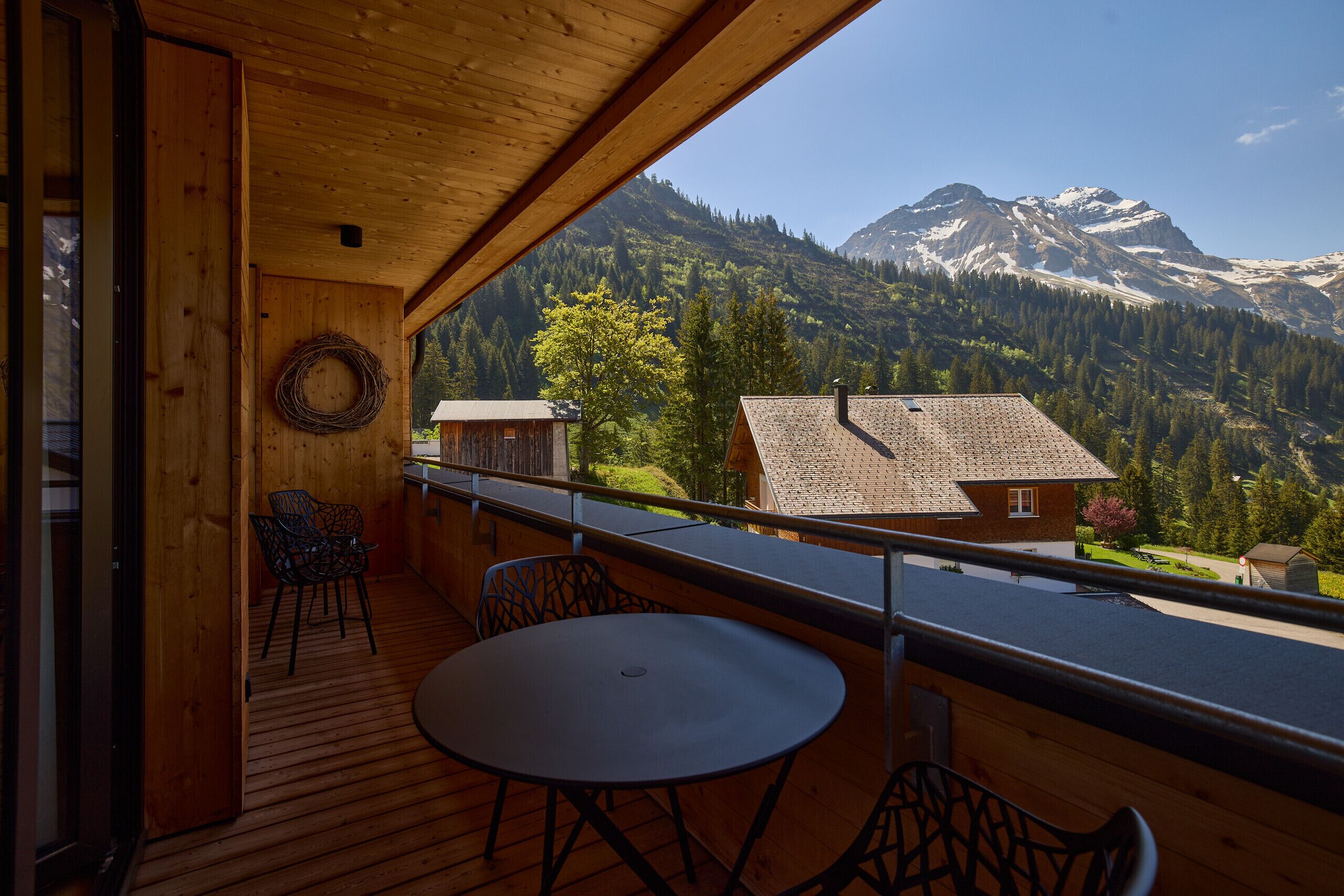 A wooden balcony with a table and chairs, overlooking a mountainous landscape with a clear sky.