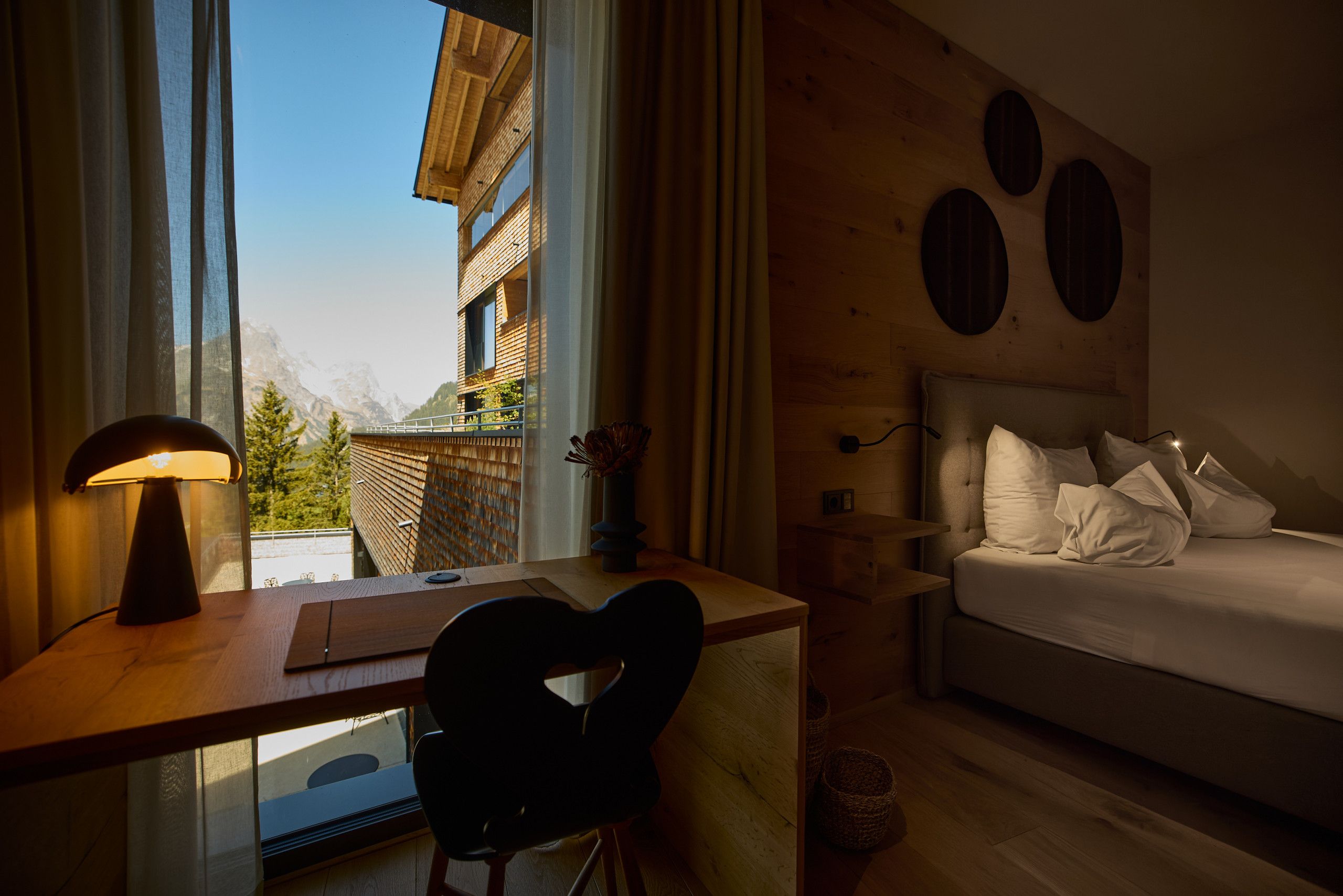 Une chambre à coucher avec un lit, un bureau doté d’une lampe et une vue sur une montagne.