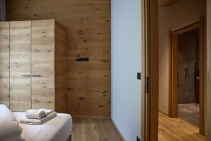 A bedroom with a wooden wardrobe, a bedside table with a rolled towel, and a shower area with a glass door. - 8005 Alpin Retreat Grand 5 (Schröcken)